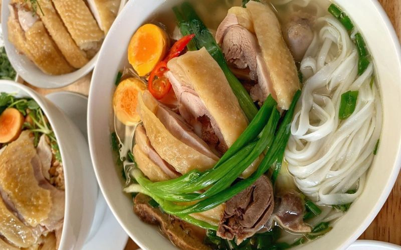 ô phở gà nóng hổi với thịt gà chặt miếng, bánh phở trắng mềm, hành lá xanh và rau thơm ăn kèm.